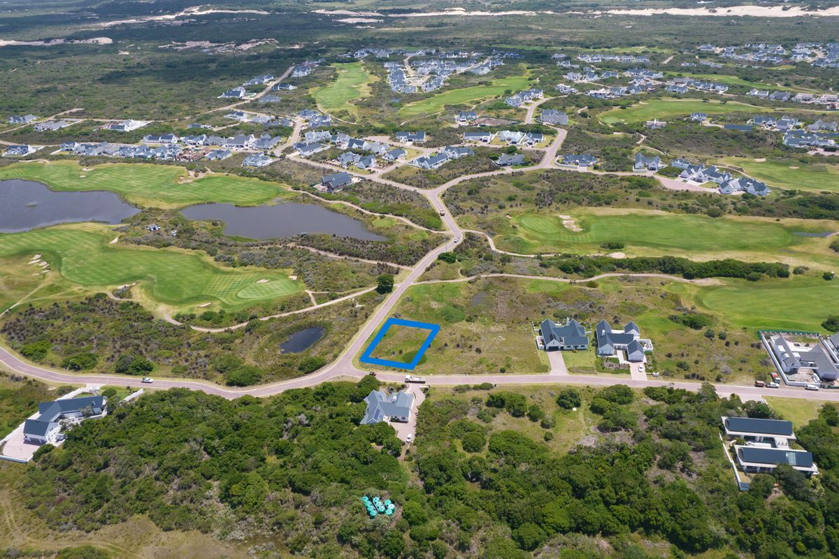 Aerial view of a vacant residential plot situated within a coastal estate, featuring paved road access and proximity to a golf course.
