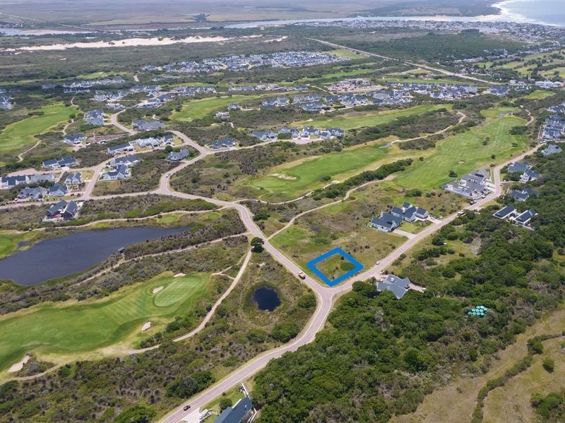 Aerial view of a vacant residential plot situated within a coastal golf estate, featuring convenient road access and surrounding natural landscape.