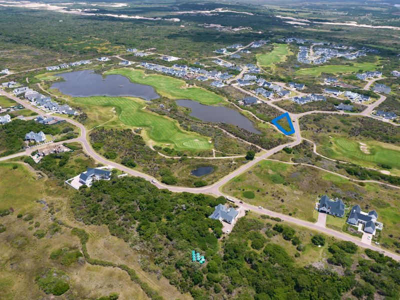 Aerial view of a residential estate featuring a golf course, natural landscape, and vacant land plots.