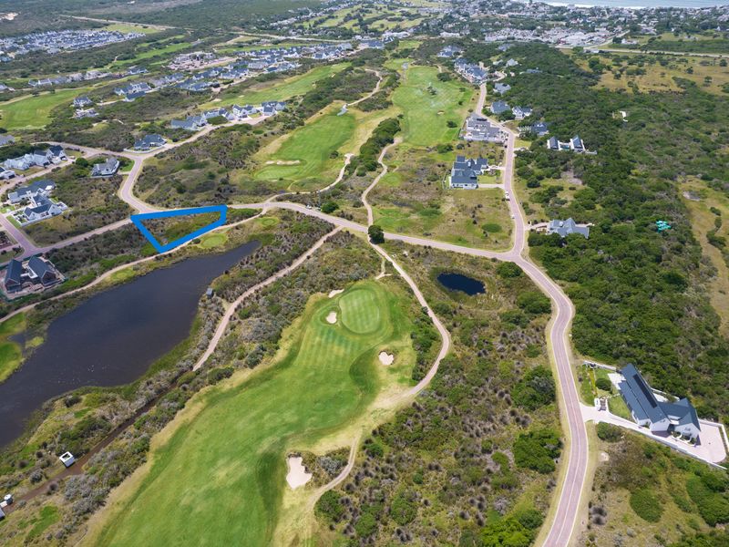An aerial view of a vacant residential plot situated within a golf estate, featuring proximity to a water body and established road infrastructure.