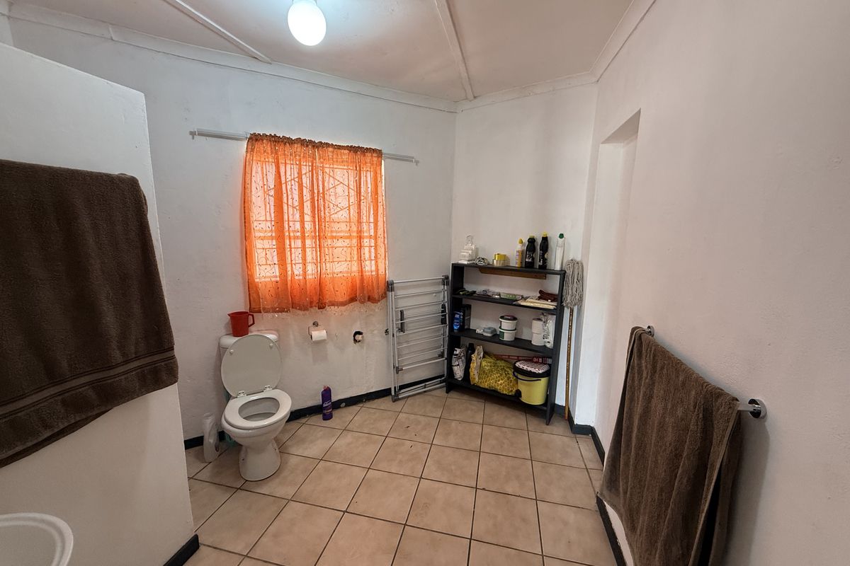 A functional bathroom featuring tiled flooring, a standard toilet, and wall-mounted towel rails, requiring some cosmetic updates to improve its overall condition.