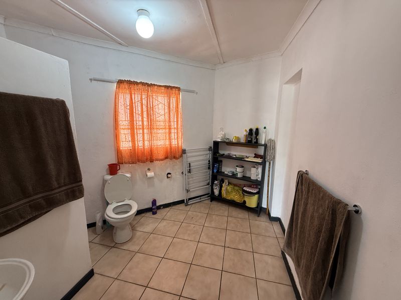 A functional bathroom featuring tiled flooring, a standard toilet, and wall-mounted towel rails, requiring some cosmetic updates to improve its overall condition.