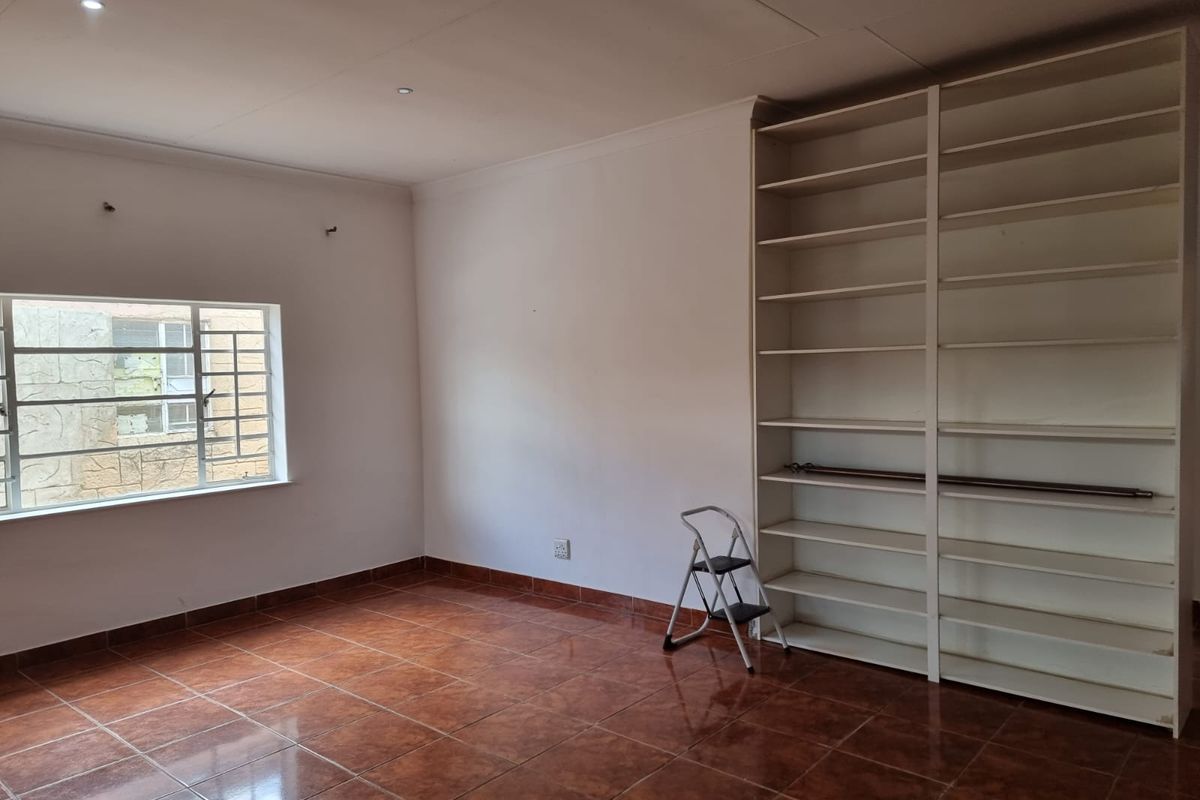 A spacious bedroom featuring large built-in shelving units, tiled flooring, and a window with security bars.