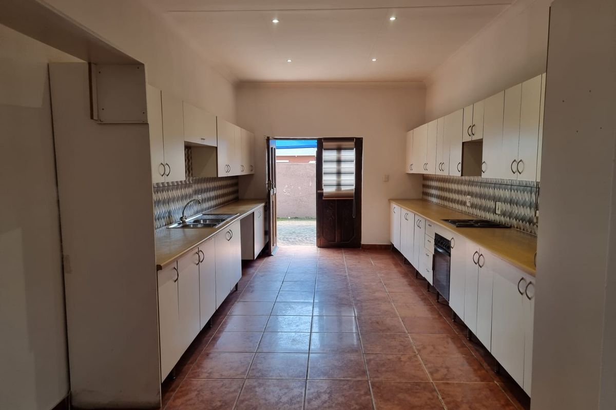 A functional galley-style kitchen featuring extensive white cabinetry, tiled flooring, a built-in oven, and a tiled backsplash with direct access to the rear exterior.
