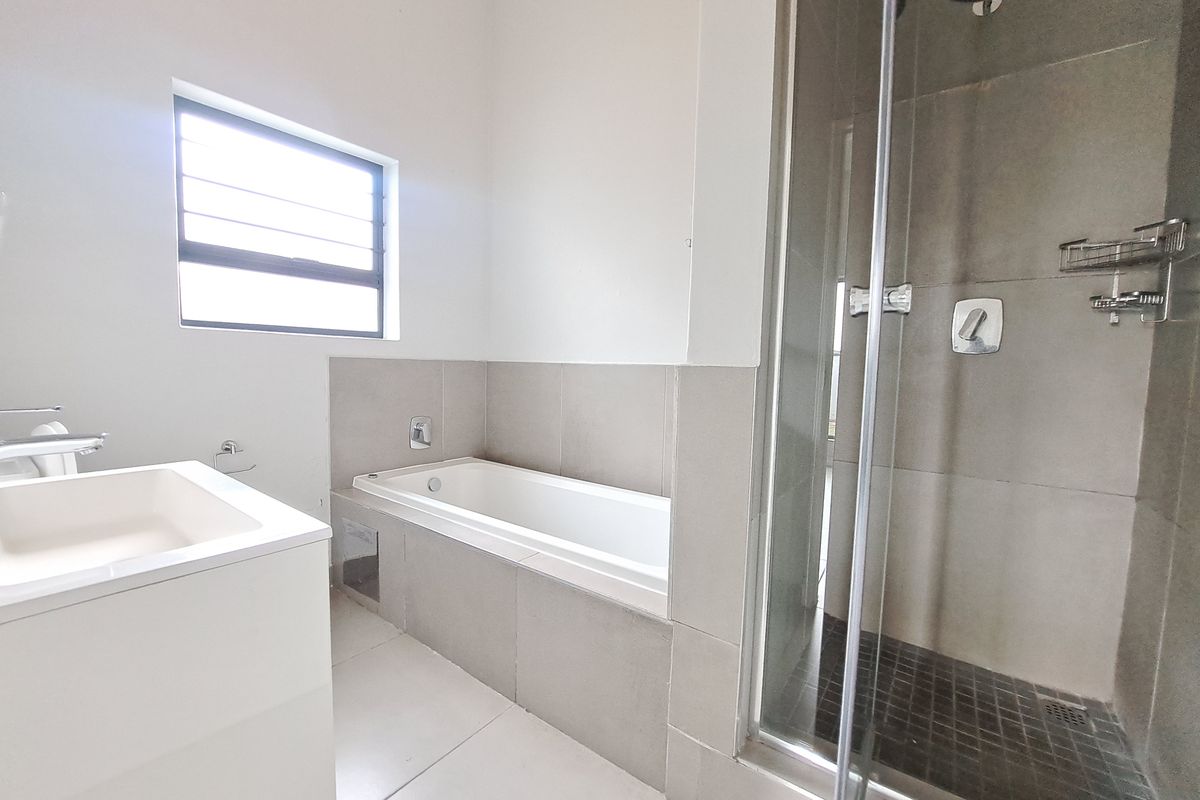 A clean, modern bathroom featuring a built-in bathtub, a separate glass-enclosed shower, and a vanity basin with neutral tiled finishes.