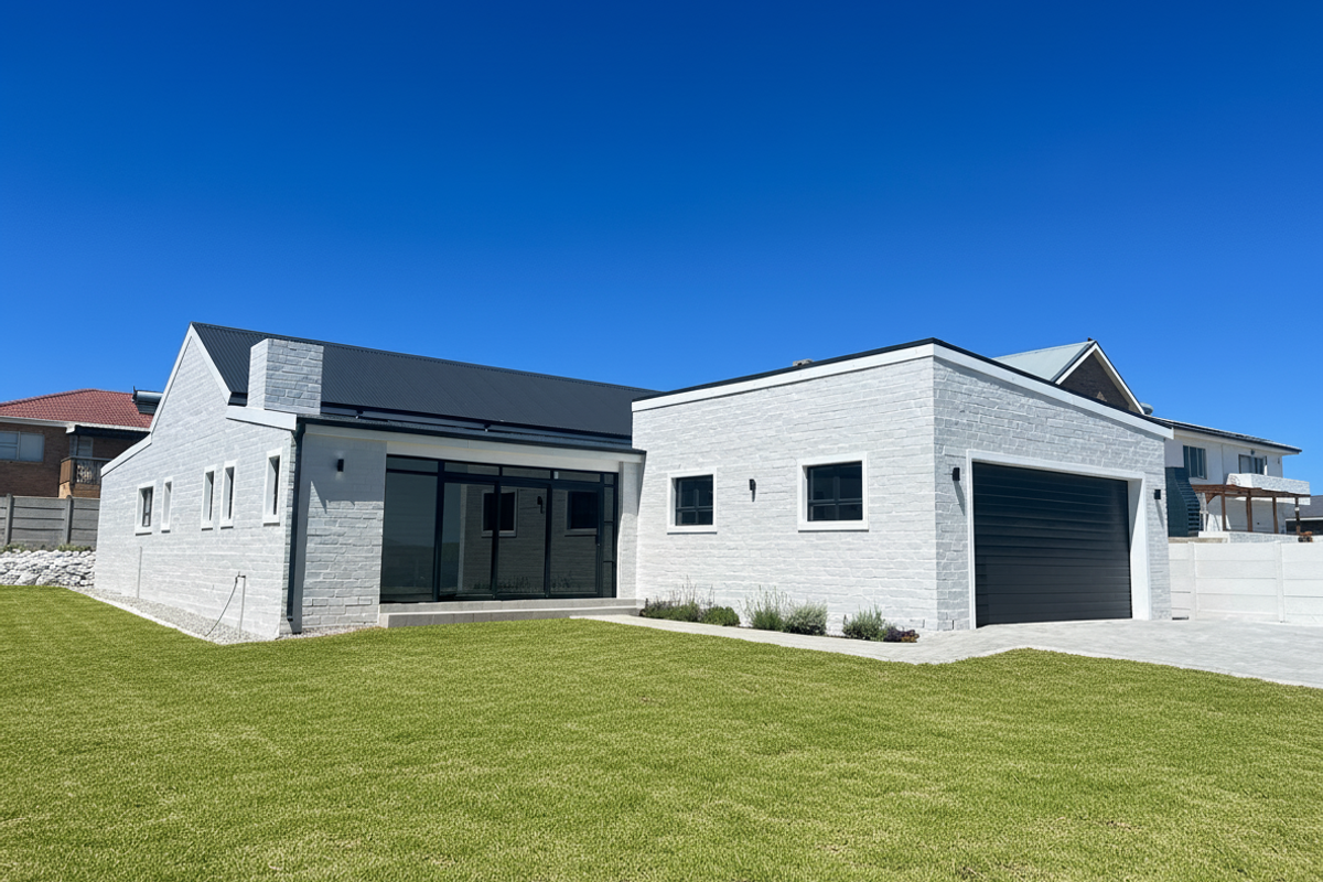 Modern single-story home featuring a painted brick exterior, black metal roofing, large sliding glass doors, and an integrated garage with a paved driveway.