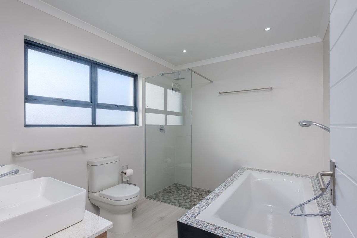 Modern bathroom featuring a glass-enclosed shower, a bathtub with mosaic tile detailing, and dual vessel sinks on a stone vanity.