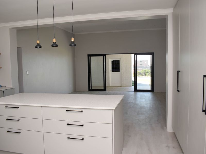 Modern open-plan kitchen and living area featuring a central island, sleek cabinetry, pendant lighting, and seamless access to the outdoor patio through sliding doors.