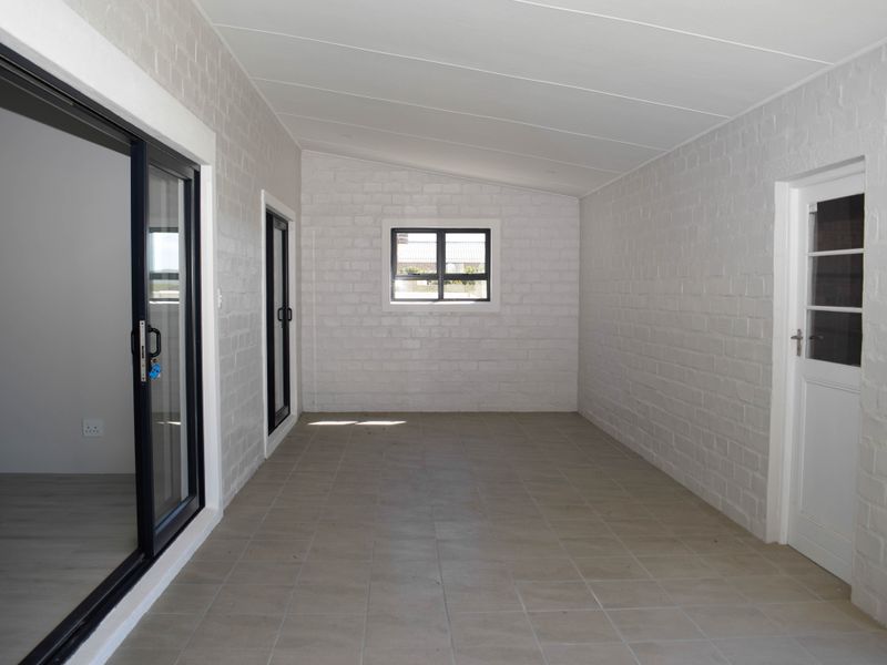 A clean, empty covered patio or sunroom featuring white painted brick walls, tiled flooring, and modern sliding glass doors leading to an adjacent space.