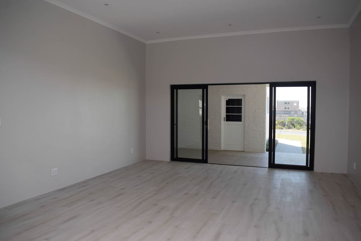 A bright, empty living room featuring modern laminate flooring, recessed downlights, and large sliding glass doors that open to an outdoor patio area.