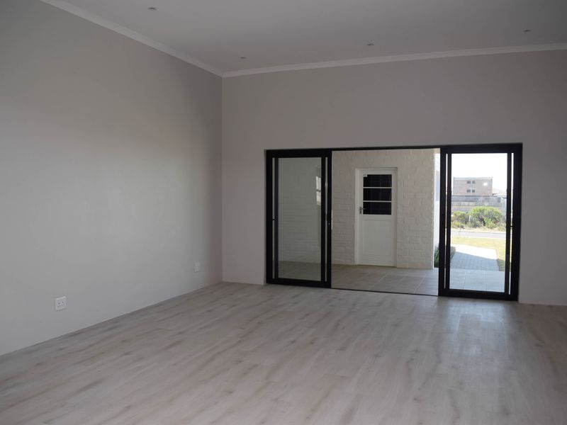 A bright, empty living room featuring modern laminate flooring, recessed downlights, and large sliding glass doors that open to an outdoor patio area.