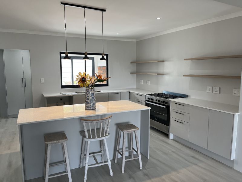 Modern kitchen featuring a central island with quartz countertops, gas stove, built-in oven, floating shelves, and contemporary cabinetry with recessed and pendant lighting.