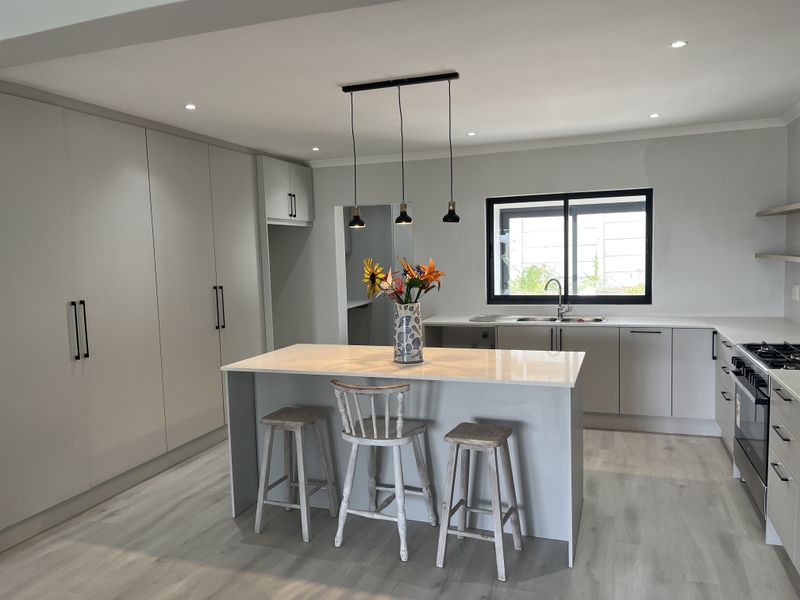 Modern kitchen featuring a central island with quartz countertops, sleek built-in cabinetry, gas stove, and contemporary pendant lighting in a bright, open space.