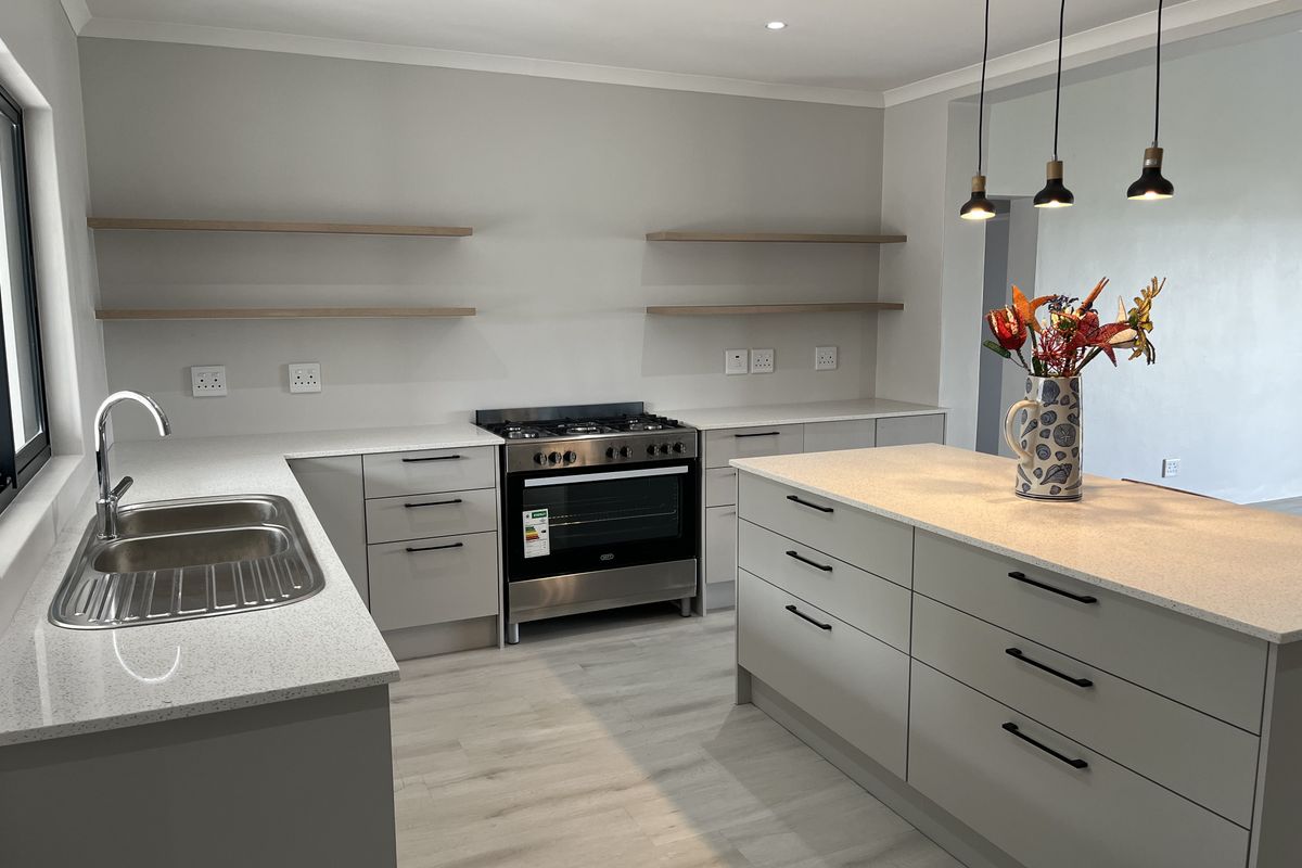 Modern kitchen featuring a central island, quartz countertops, floating shelving, and a stainless steel gas stove, finished with contemporary cabinetry and pendant lighting.