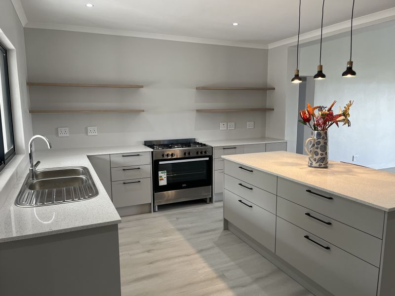 Modern kitchen featuring a central island, quartz countertops, floating shelving, and a stainless steel gas stove, finished with contemporary cabinetry and pendant lighting.