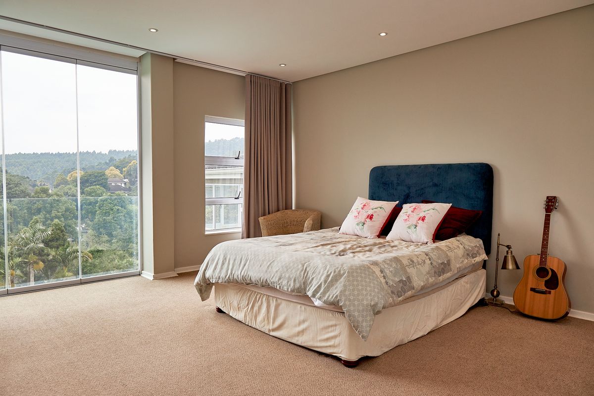 Spacious bedroom featuring neutral walls, plush carpeting, recessed lighting, and large floor-to-ceiling glass doors offering expansive views.
