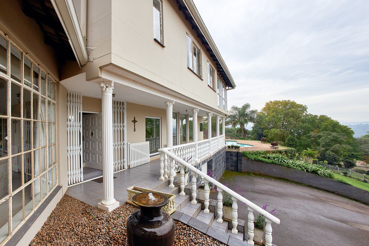 Rear exterior view featuring a covered patio with classical columns, tiled flooring, security gates, and a swimming pool overlooking the garden.