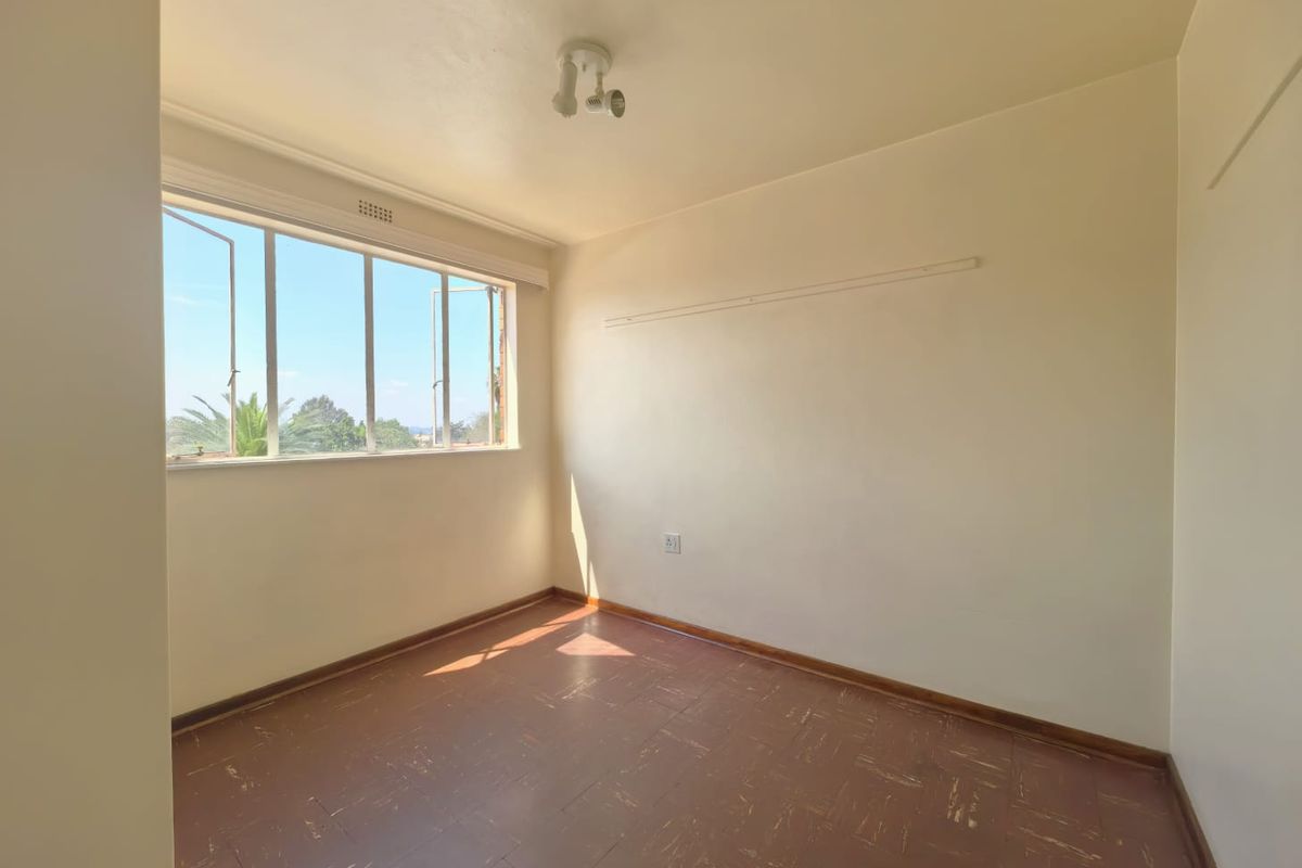 A vacant bedroom featuring original parquet flooring, a large window with natural light, and a simple ceiling-mounted light fixture.