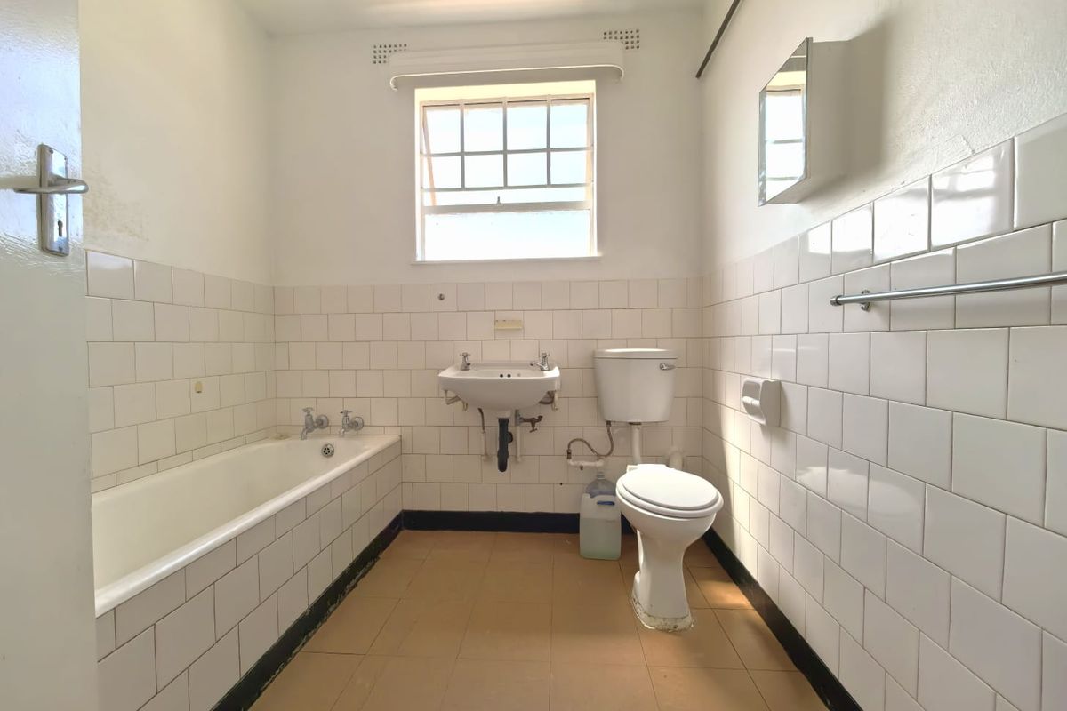 A dated bathroom featuring a standard bathtub, wall-mounted basin, and toilet with white subway-style wall tiling and original floor finishes.