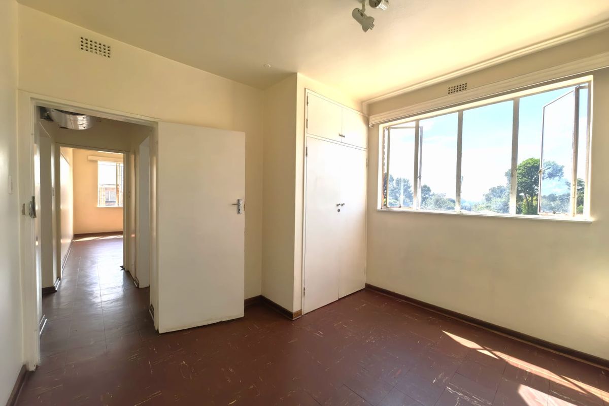 A bright, empty bedroom featuring original parquet flooring, built-in storage cupboards, and large windows allowing for ample natural light.