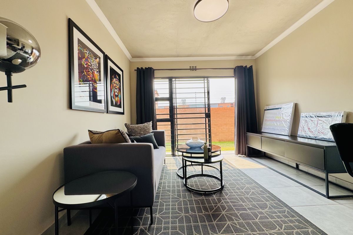A well-lit living room featuring tiled flooring, a ceiling-mounted light fixture, and a sliding glass door with security gate leading to the exterior.