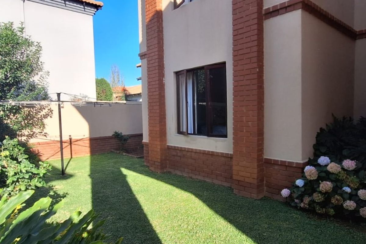 A view of the rear garden area featuring a well-maintained lawn, brick-accented exterior wall, and established garden beds.