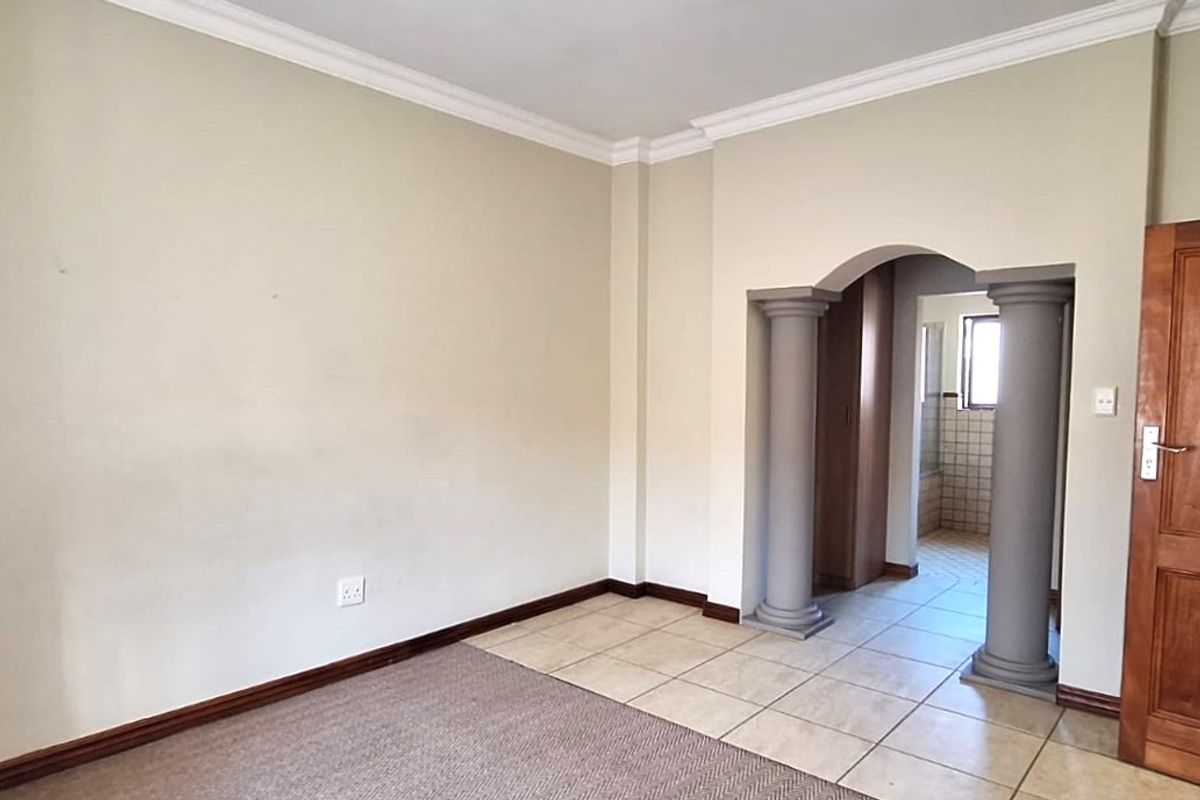 An empty bedroom featuring a decorative arched entryway with columns, neutral wall tones, and a combination of carpet and tile flooring.
