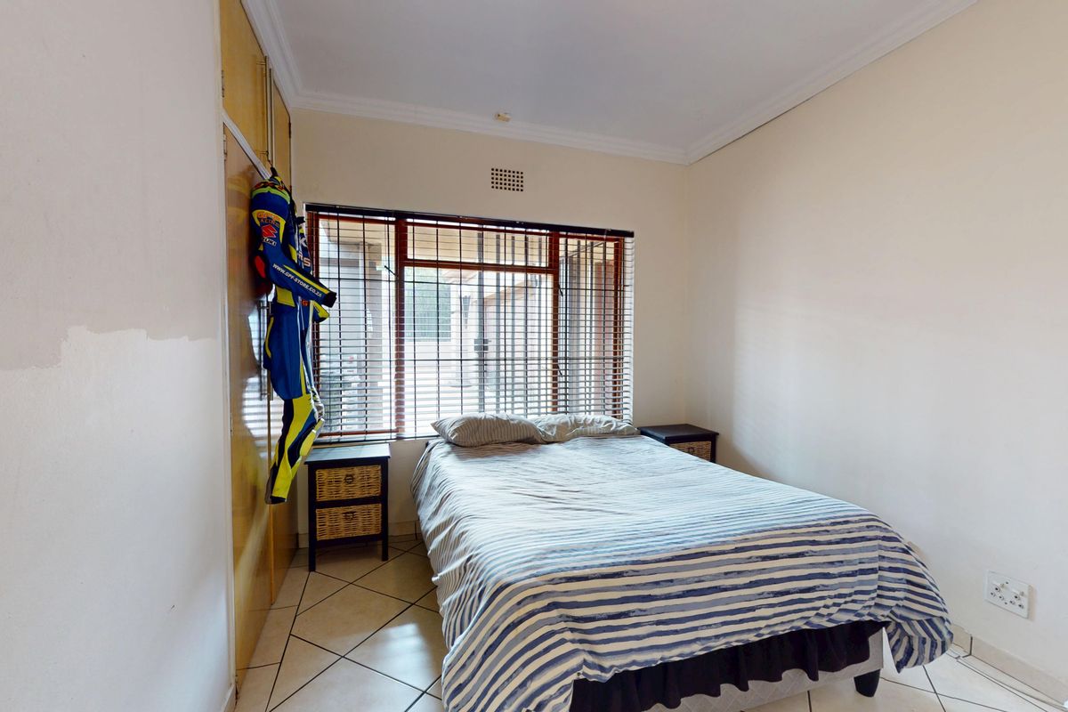 A bedroom featuring tiled flooring, built-in cupboards, and window security bars. The room requires cosmetic updates to the wall finishes.