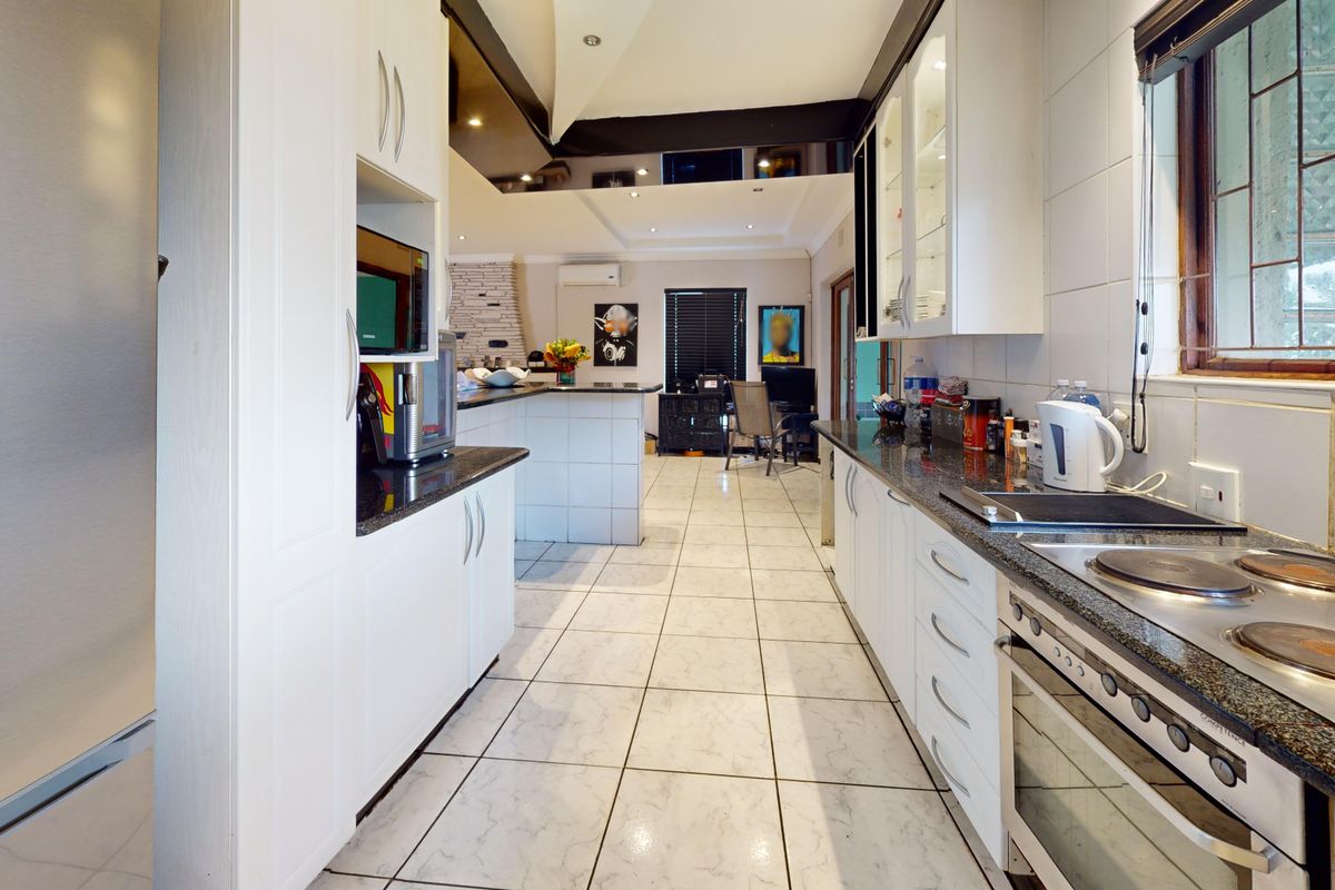 A functional kitchen featuring white cabinetry, granite countertops, built-in oven and hob, and tiled flooring, with an open-plan layout leading to the living area.