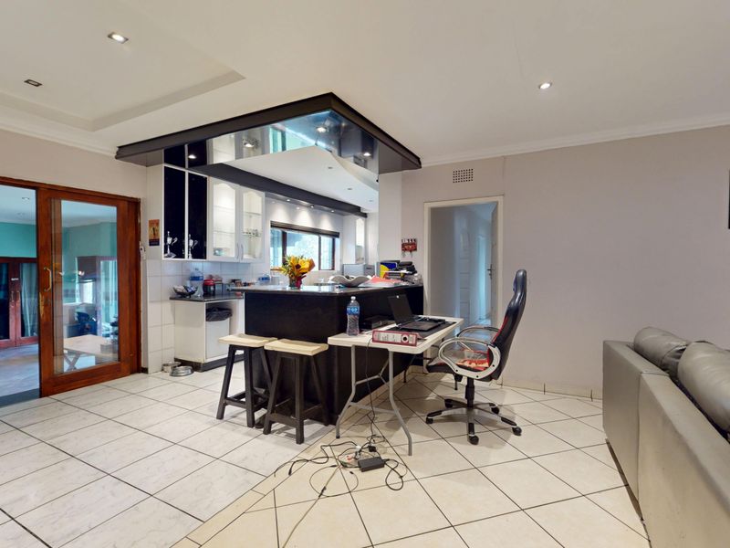 Open plan living area featuring a central kitchen island, tiled flooring, and recessed lighting, with a sliding door leading to an adjacent room.
