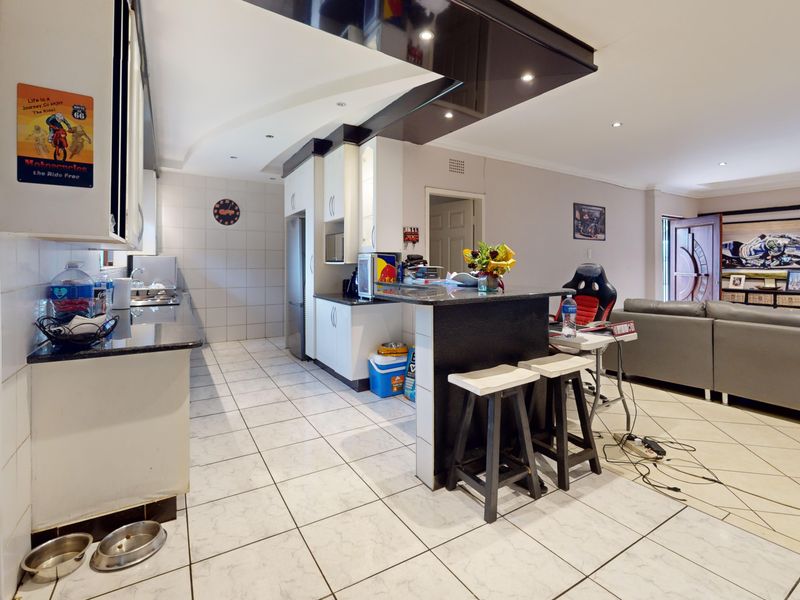 Open plan kitchen and living area featuring tiled flooring, granite countertops, and a breakfast bar with modern recessed lighting.