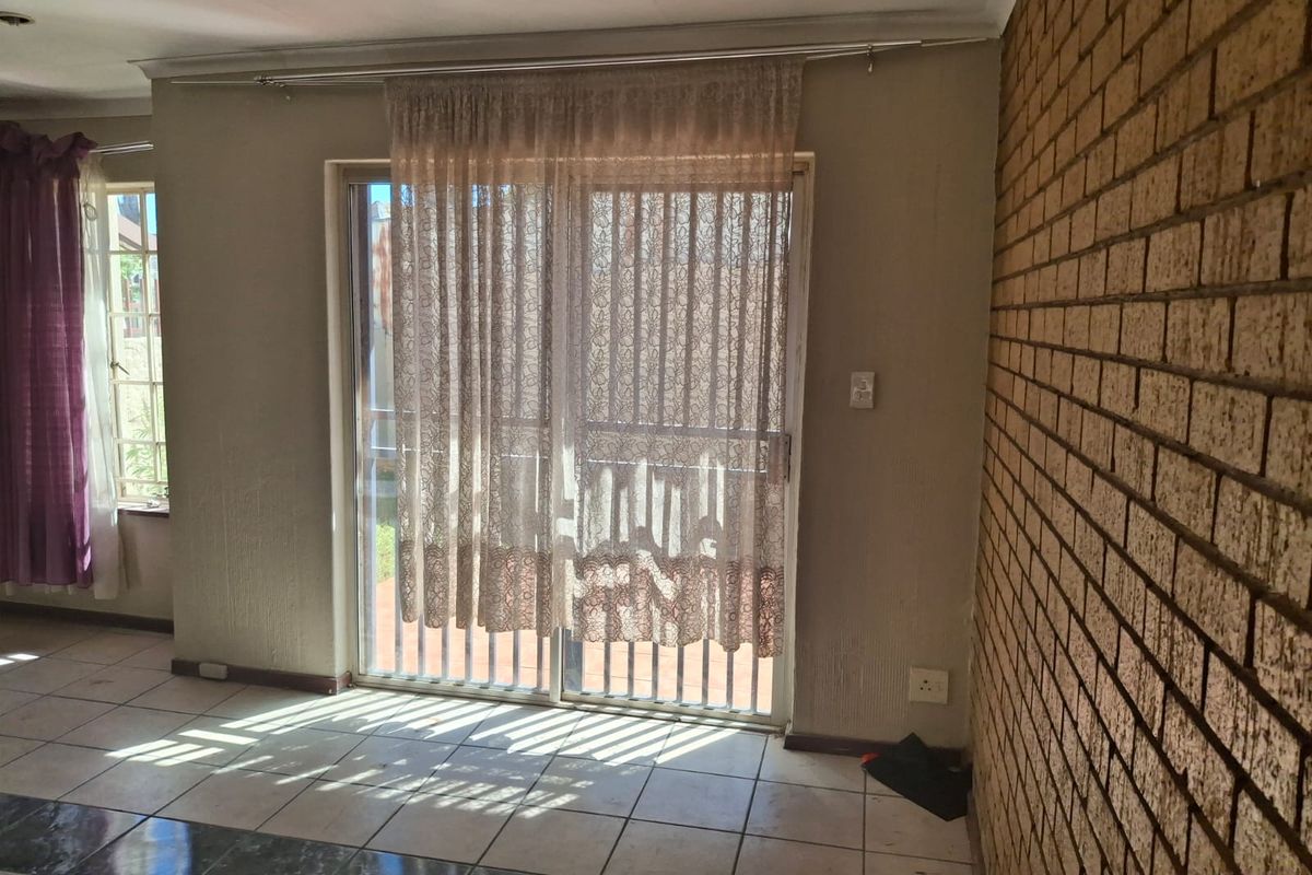 Living area featuring a brick feature wall, tiled flooring, and sliding glass doors providing access to the outdoor patio area.