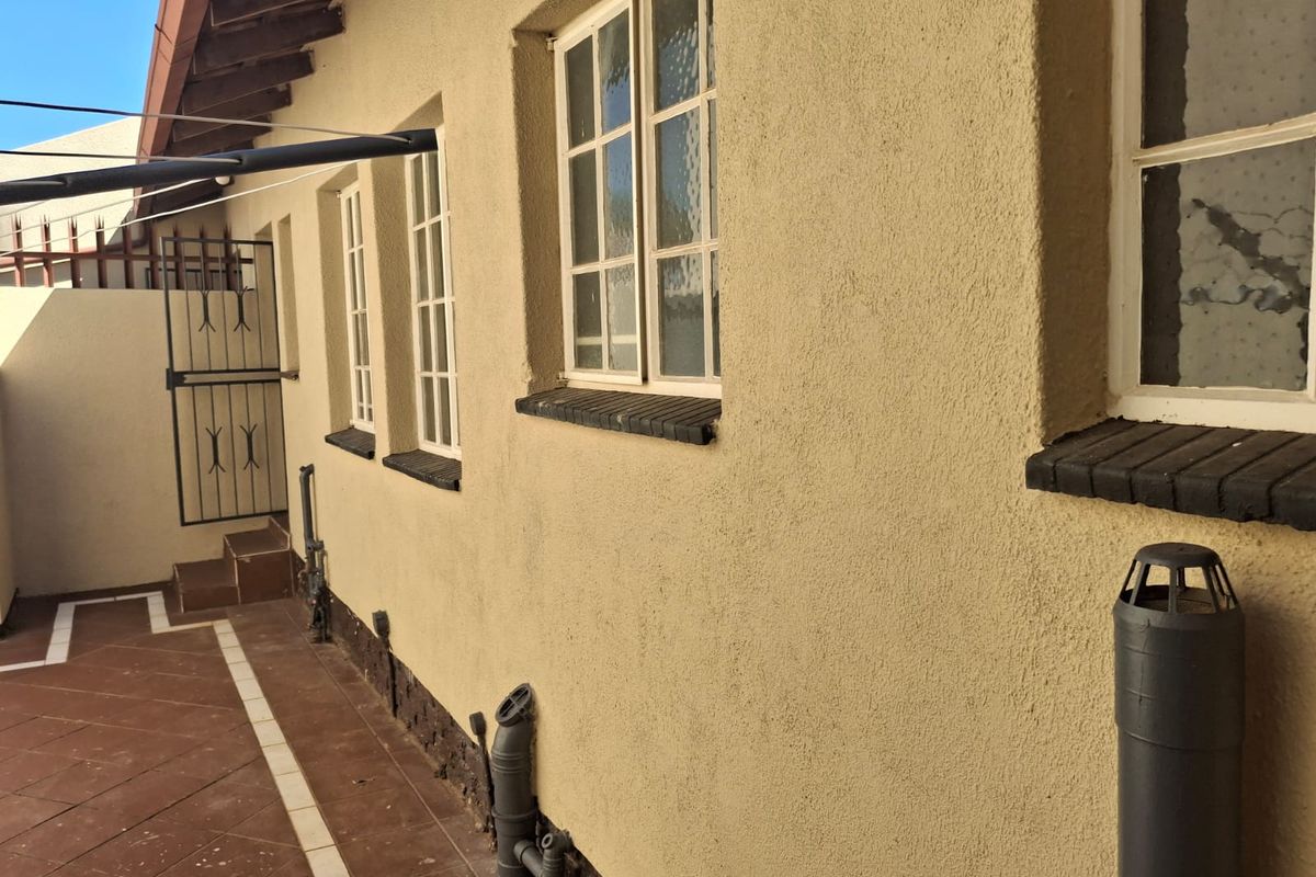 A view of the rear exterior elevation featuring a paved walkway, textured wall finish, and multiple window openings with brick sills.