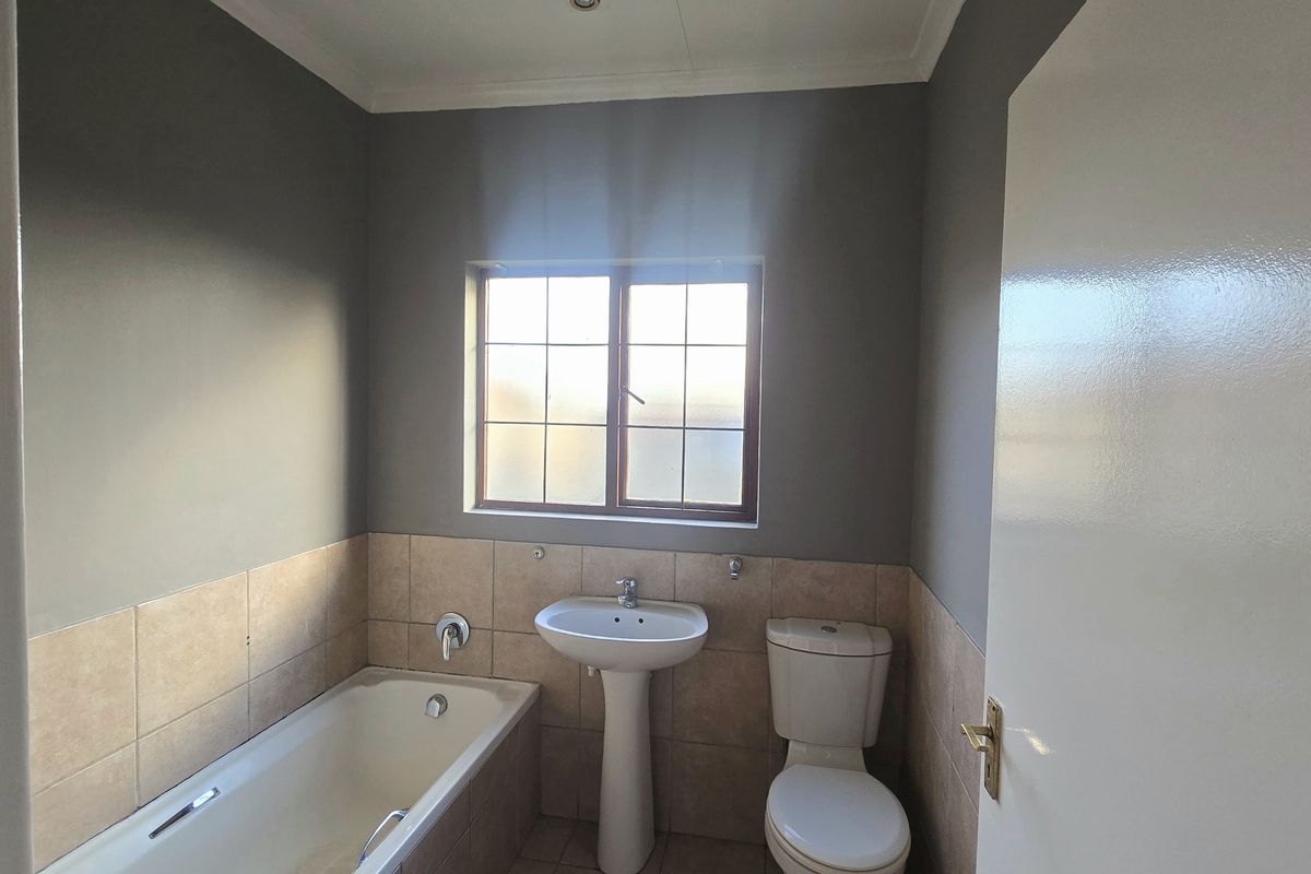 A functional bathroom featuring a pedestal basin, toilet, and bathtub with neutral wall paint and tiled splashbacks.
