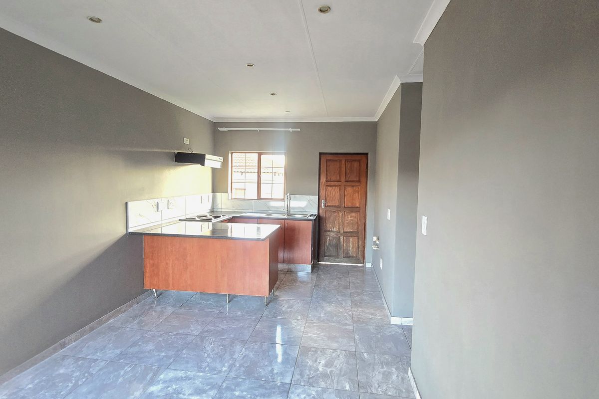 A functional kitchen featuring built-in cabinetry, a hob with an extractor fan, tiled flooring, and a tiled splashback in a neutral color scheme.