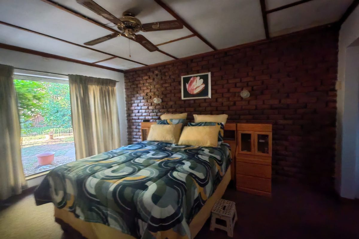 A bedroom featuring an exposed brick feature wall, exposed beam ceiling, ceiling fan, and a sliding glass door providing access to the garden.