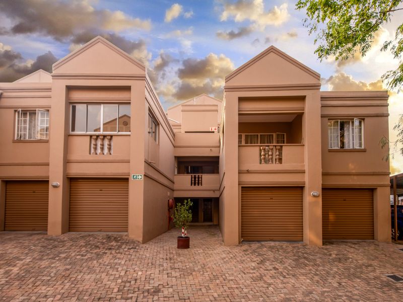 Front elevation of a multi-unit apartment complex featuring paved driveway access, multiple roller shutter garage doors, and upper-level balconies with balustrades.