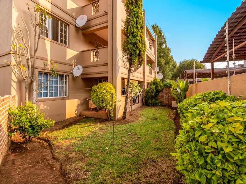 Rear view of the apartment building featuring private balconies, a small garden area, and perimeter security with electric fencing.