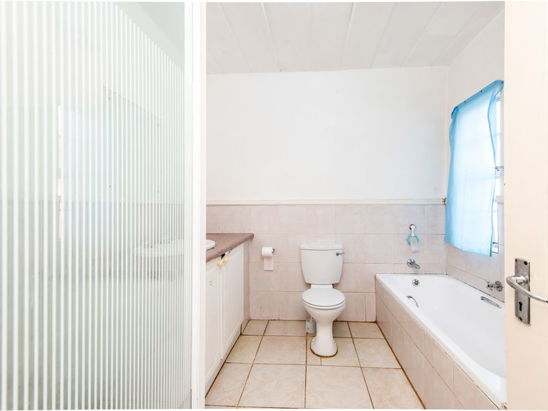 A functional bathroom featuring a built-in vanity, toilet, and bathtub with tiled flooring and wall splashbacks.