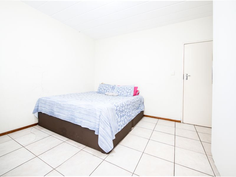 A simple bedroom featuring tiled flooring and a panelled ceiling, offering a blank canvas for potential interior updates.