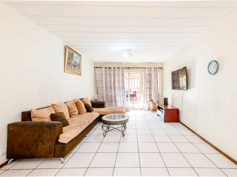 A living room featuring tiled flooring, a sliding glass door leading to the exterior, and panelled ceiling. Walls show visible signs of wear and marking.