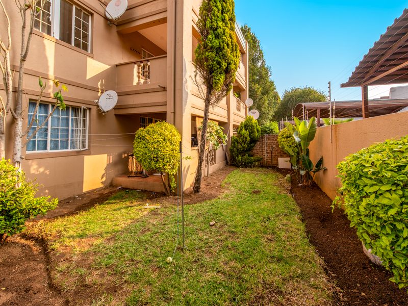 Rear view of the apartment building featuring a private garden area, boundary wall with electric fencing, and access to upper-level balconies.