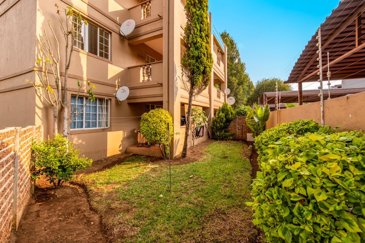 Rear view of the apartment building featuring private balconies, a small garden area, and perimeter security with electric fencing.