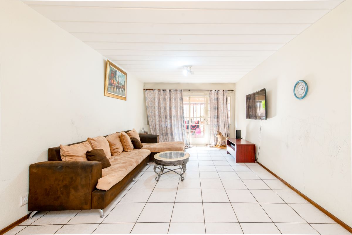 A living room featuring tiled flooring, a sliding glass door leading to the exterior, and panelled ceiling. Walls show visible signs of wear and marking.