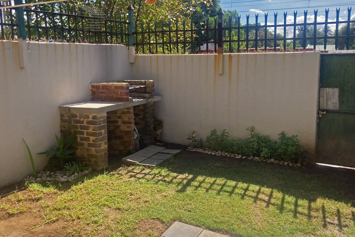 A private rear courtyard featuring a built-in brick braai area, perimeter wall with security fencing, and a small garden space.
