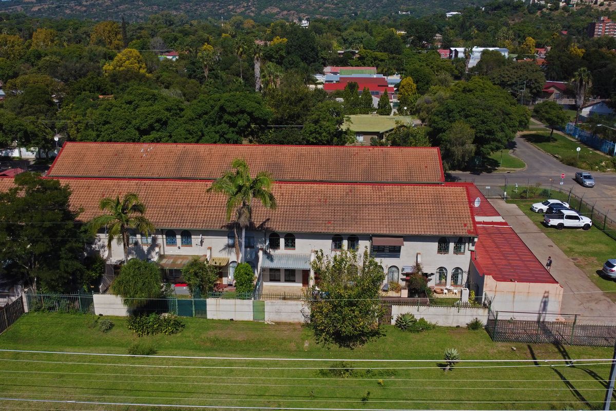 Aerial view of a townhouse complex featuring a long terracotta tiled roof, perimeter fencing, and surrounding landscaped grounds.