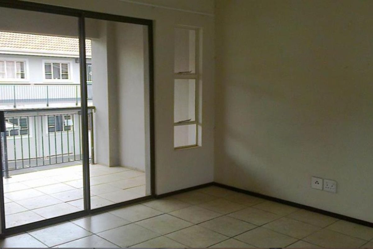 An empty living area featuring tiled flooring, a vertical window, and sliding glass doors that open onto a private balcony.