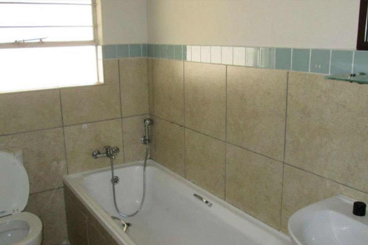 A functional bathroom featuring a bathtub with a handheld shower attachment, a toilet, and a wall-mounted basin with neutral-toned wall tiles.