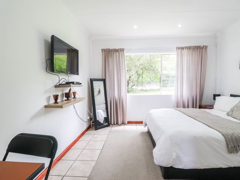 A bright bedroom featuring tiled flooring, recessed downlighting, and a window with security bars, offering a clean and functional living space.