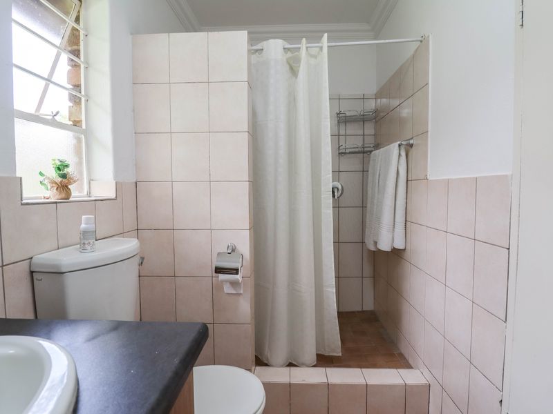 A functional bathroom featuring a shower cubicle, toilet, and vanity basin with neutral wall tiling and natural light from a side window.